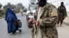 A woman wearing a burqa with a child walk past Taliban fighters along a roadside in Jalalabad, Afghanistan. (file photo)