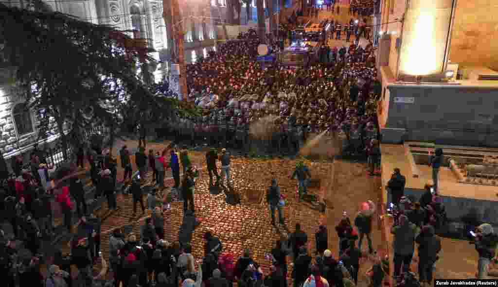 A wall of police faces protesters on a street that leads to the rear entrance of Georgia's parliament building (seen on right). 