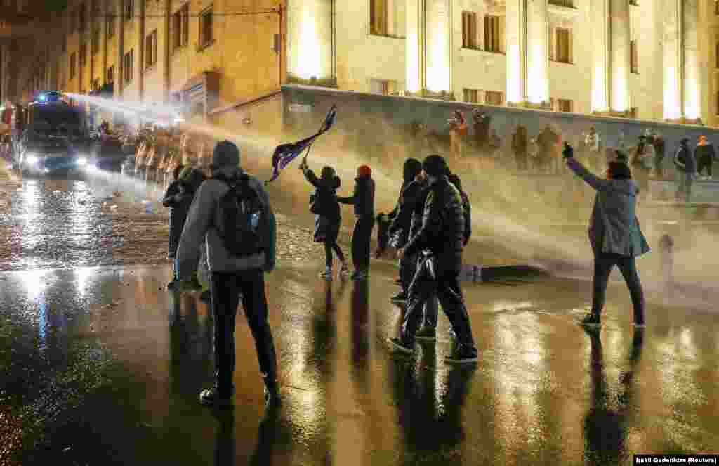 Protesters, one waving an EU flag, are sprayed by a water cannon. 