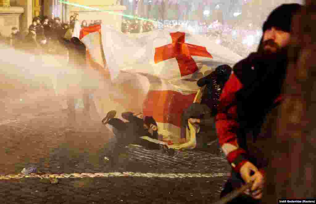 A protester is toppled as he is hit by a water cannon on a street that leads to the rear entrance of the parliament. 