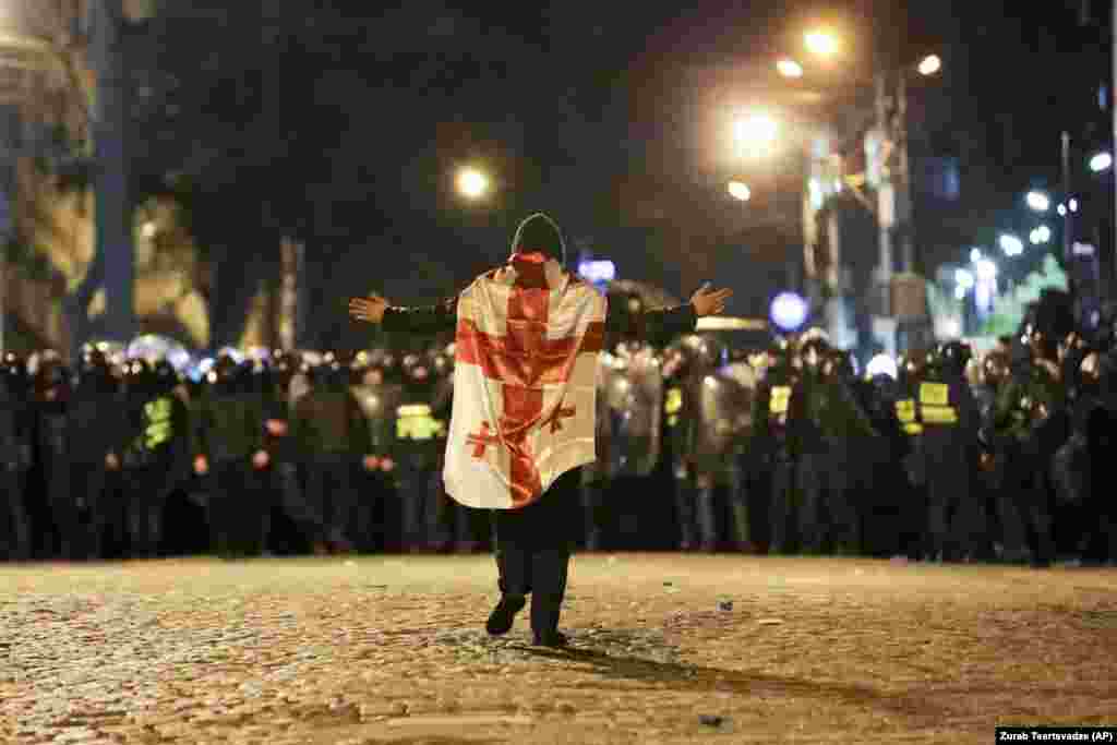 A protester wearing the Georgian flag walks toward a line of riot police outside the Georgian parliament building on March 7. Violent protests broke out after legislators gave preliminary backing to a bill that would require organizations operating in Georgia that receive more than 20 percent of their funding from abroad to register as a "foreign agent." 