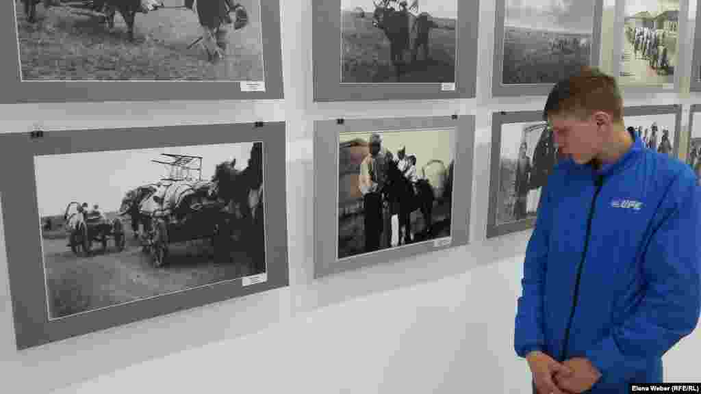 Подросток, приехавший на фотовыставку вместе с группой школьников, внимательно разглядывает фотографии, вчитываясь в их описание. 