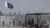 Afghan and Pakistani nationals walk through a security barrier to cross the border as the Pakistani and Taliban flags fly at the Pakistan-Afghanistan border crossing point in Chaman.