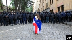 A demonstrator draped in the Georgian national and EU flags stands in front of a police cordon during an opposition protest in Tbilisi. (file photo)