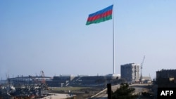 An enormous Azerbaijani flag flies above the Caspian Sea shoreline in Baku.